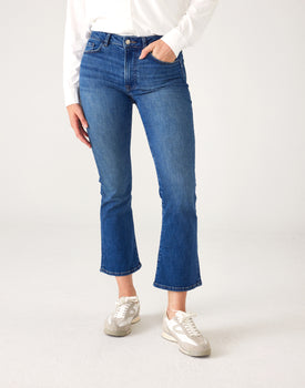lower body of Woman wearing Mersea Infinity blue Nomad cropped mini boot-cut jeans standing against white background