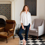 Woman showcasing Mersea moody blue Nomad cropped mini boot-cut  jeans standing in a living room