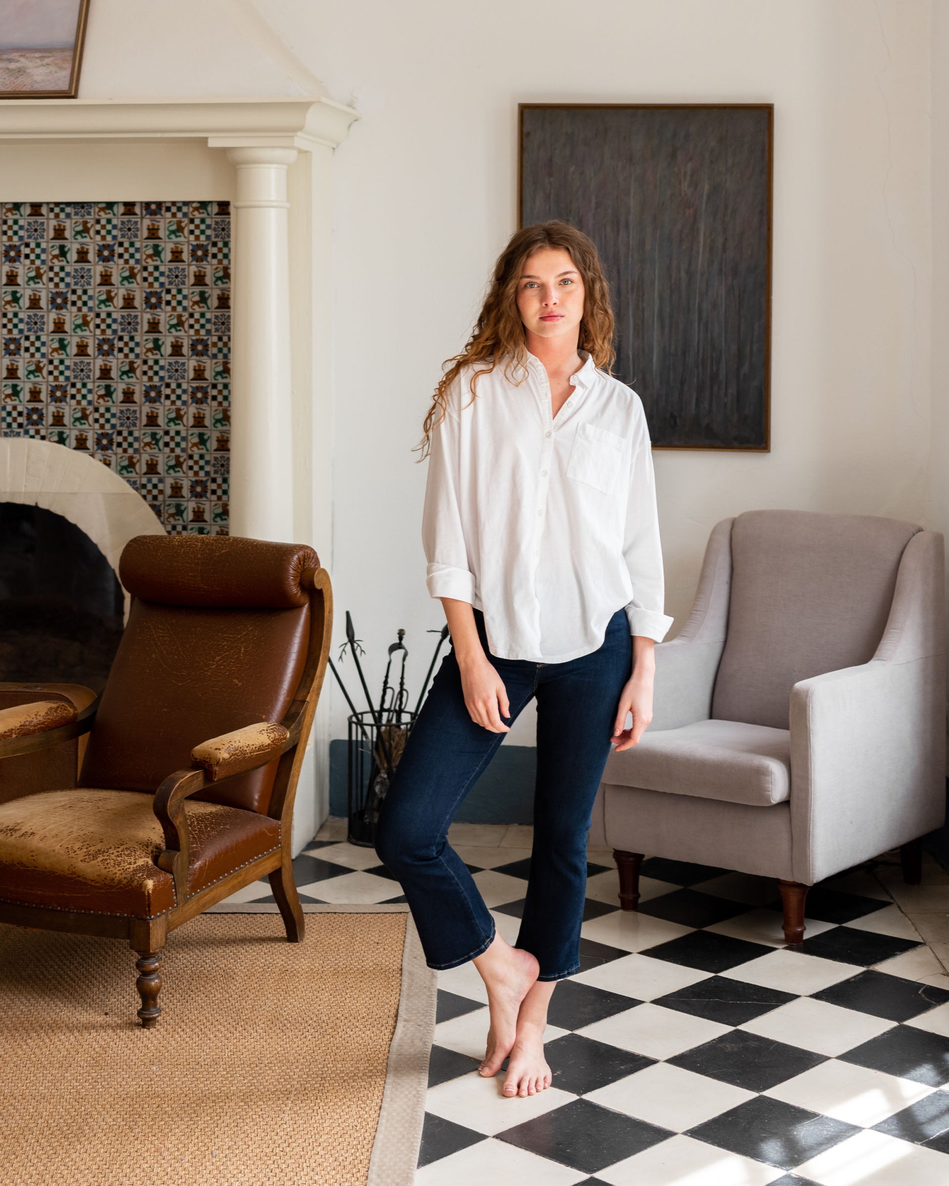 Woman showcasing Mersea moody blue Nomad cropped mini boot-cut  jeans standing in a living room