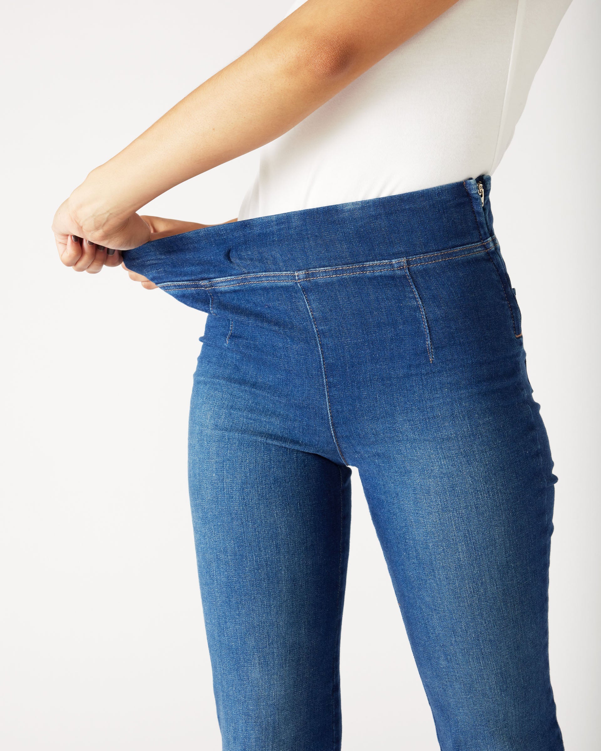 closeup of stretch waist on Mersea Nomad cadet blue denim full length boot-cut jeans against white background
