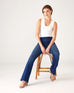 Woman showcasing Mersea Nomad cadet blue denim full length boot-cut jeans sitting on stool