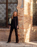 Woman showcasing Mersea Nomad black denim full length boot-cut jeans standing in front of brick building