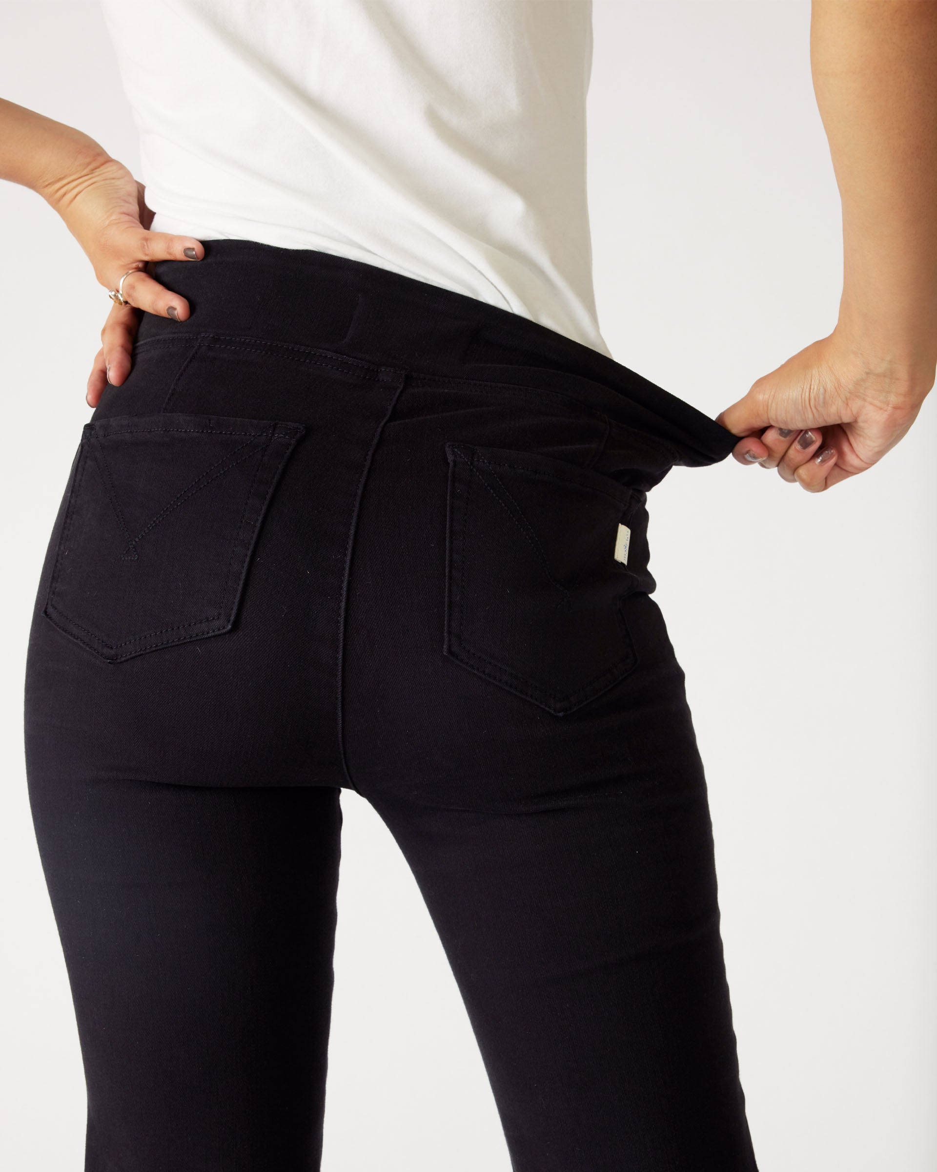 Rear view of Woman showcasing stretch waist on  Mersea Nomad black denim full length boot-cut jeans on a white background