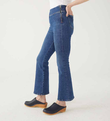 female wearing medium wash pull up boot cut jeans with a side zipper and clogs on white background