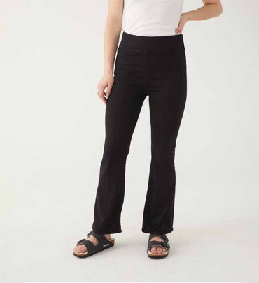 female wearing black boot cut pull on jeans with white tank and black birks on a white background