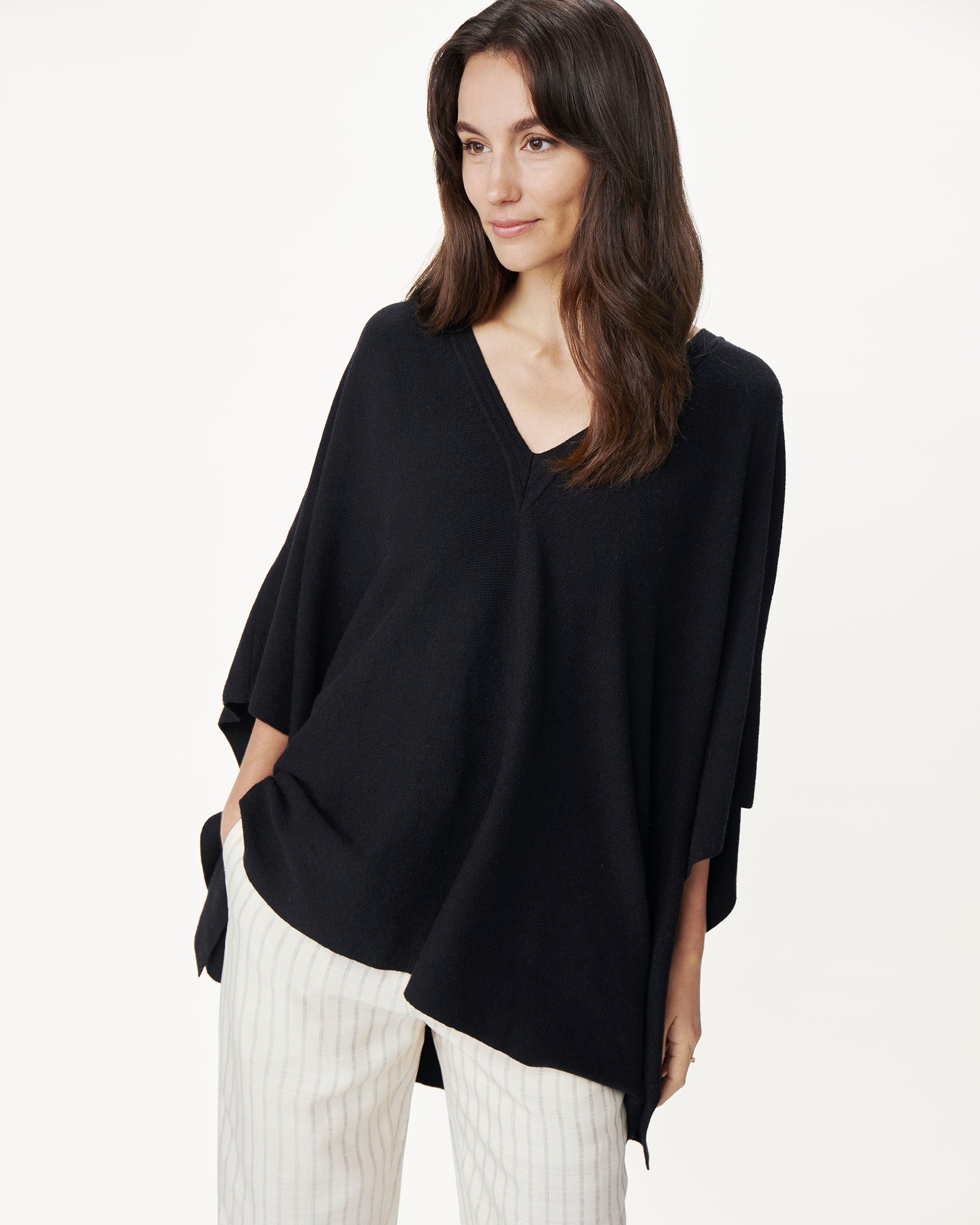female wearing black v neck poncho with white pants on a white background