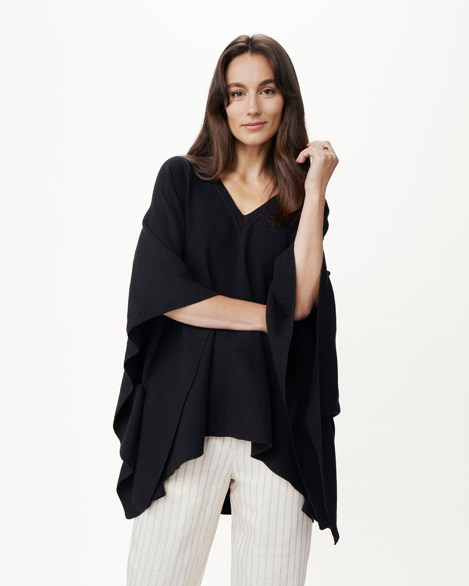 female wearing black v neck poncho with white pants on a white background
