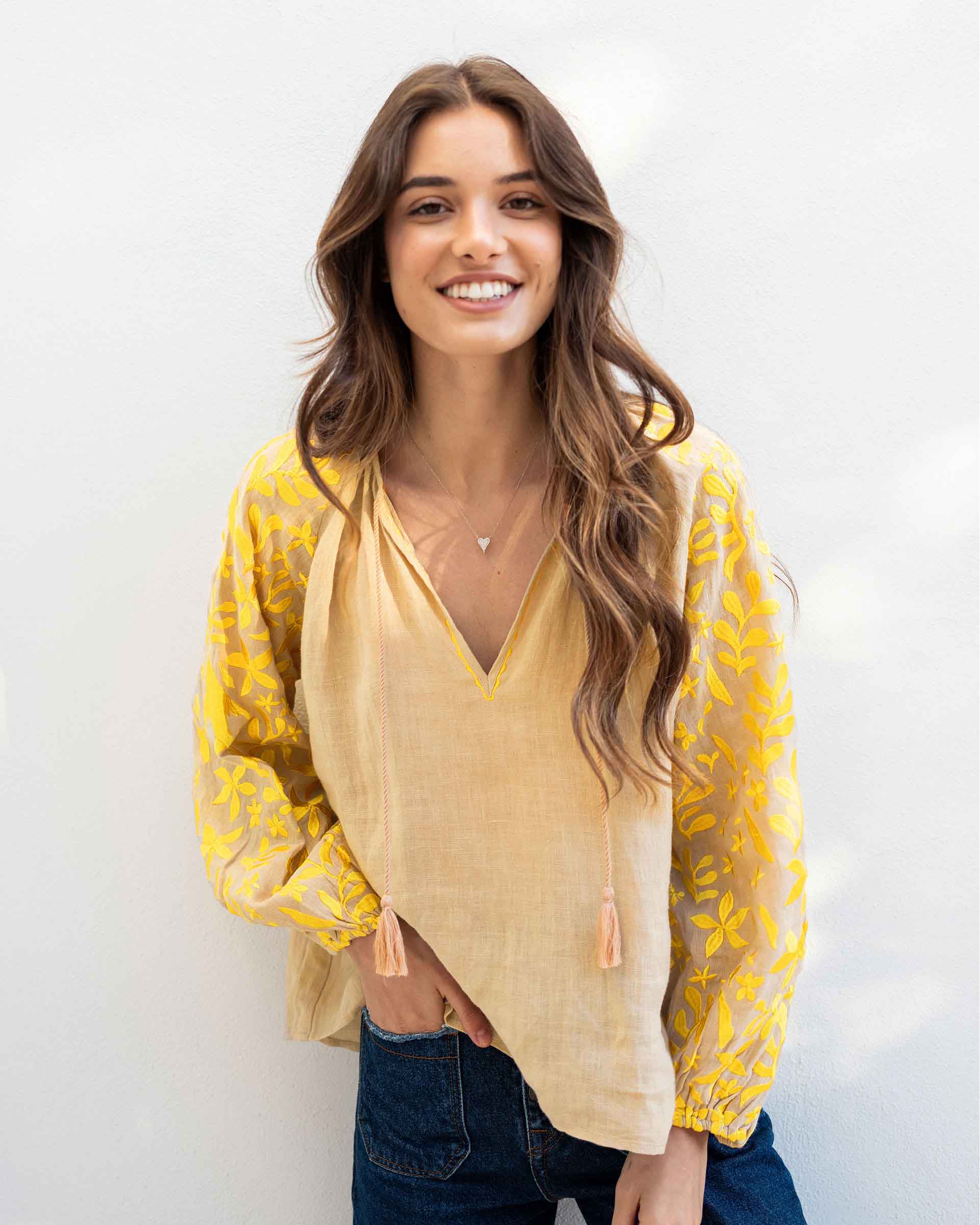 female wearing tan blouse with yellow embroidery on a white background 