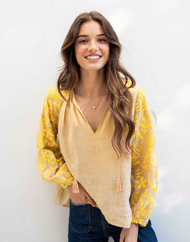 female wearing tan blouse with yellow embroidery on a white background 
