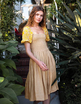 Female wearing a beige and yellow dress with embroidered puff sleeves in front of pants