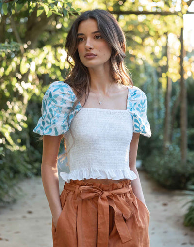 Female wearing a white top with embroidered blue details on puff sleeves