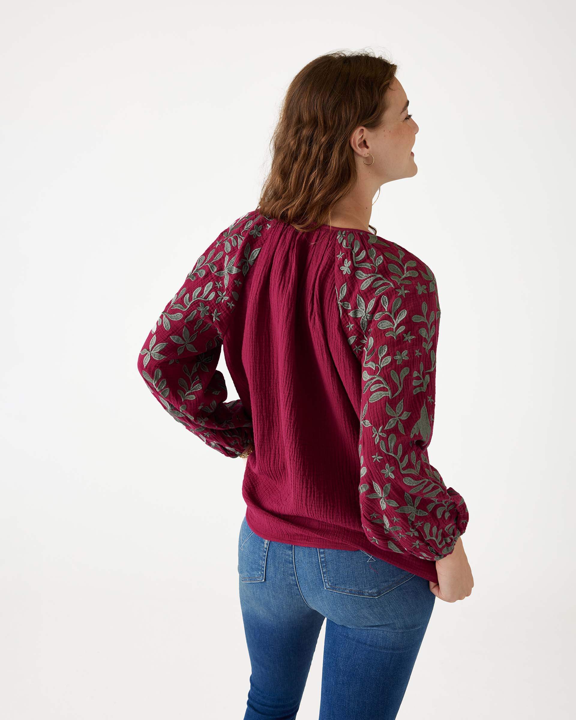 rearview of female wearing Mersea berry v-neckline blouse with embroidered sleeves and tassel ties standing on white background