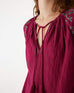 closeup of v-neck on female wearing Mersea berry v-neckline blouse with embroidered sleeves and tassel ties standing on white background