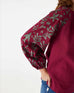 closeup of embroidered sleeves on Mersea berry v-neckline blouse with tassel ties standing on white background