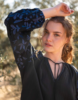 closeup of embroidered sleeve on female wearing Mersea black v-neckline blouse with tassel ties with arm raised
