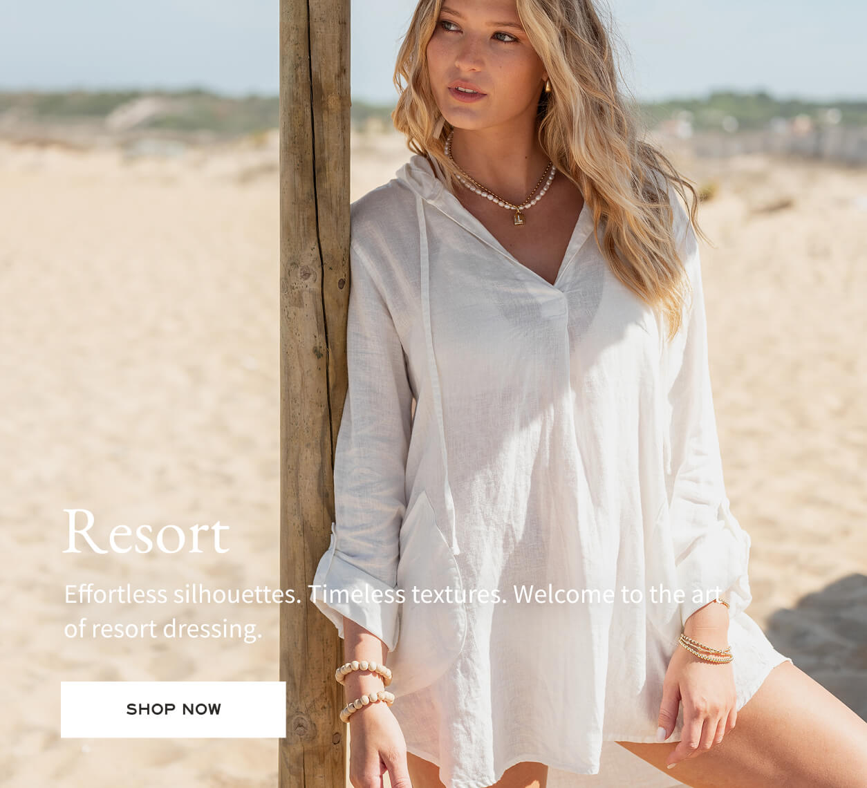 Resort - Effortless silhouettes. Timeless textures. Welcome to the art of resort dressing. - text overlay a women on the beach in a white linen tunic