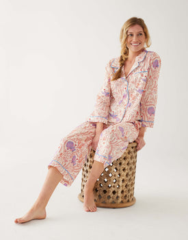 woman wearing mersea matching pajama set with peacock vines print sitting on stool