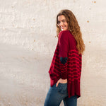 female wearing blue jeans red striped sweater with navy heart elbow patch on a white wall