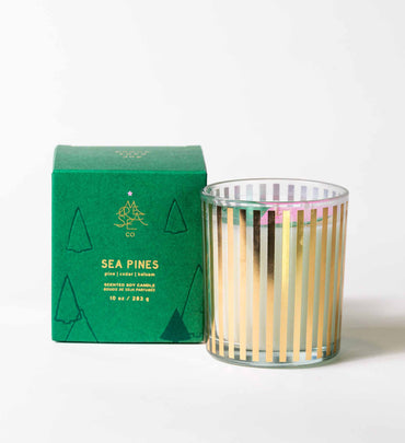 sea pines glass candle with gold stripes next to green box on a white background