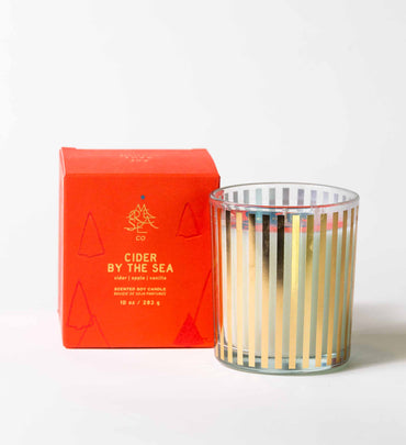 cider by the seas glass candle with gold stripes next to red box on a white background