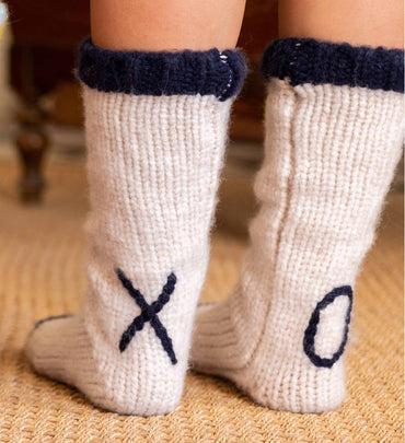 female wearing white slipper socks with black lining and XO on back of ankles standing on carpet