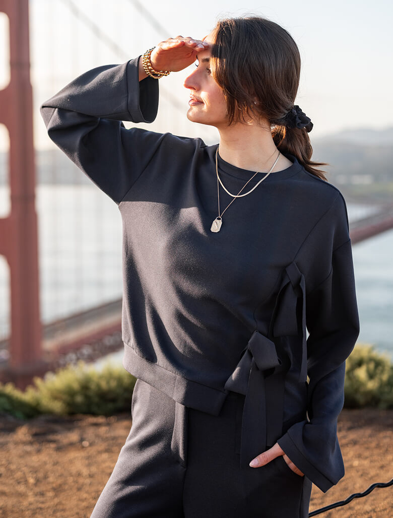 Person wearing a black outfit with a blurred background of a bridge and water.