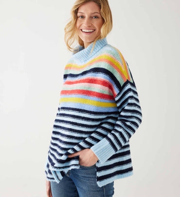female wearing multi striped sweater with wide turtleneck over jeans on a white background
