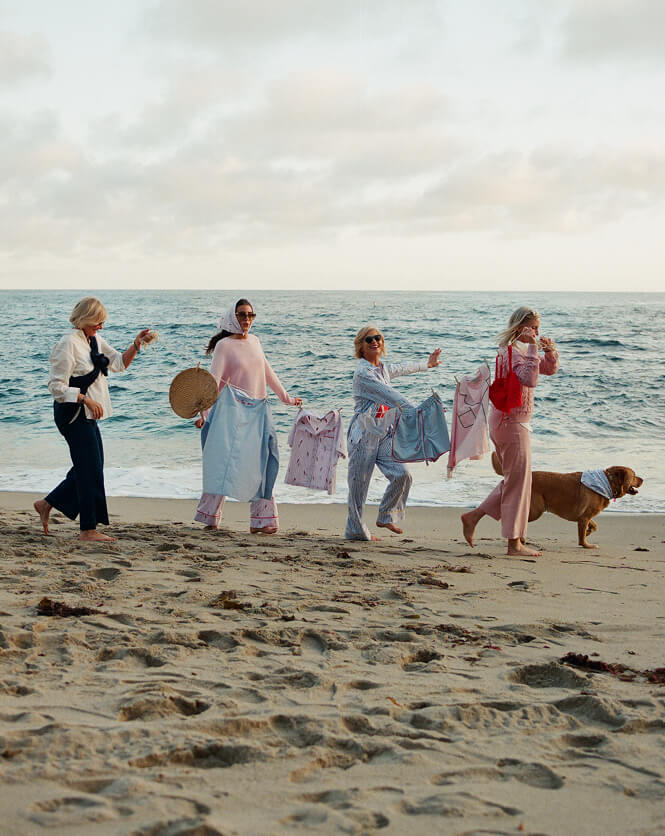 Four women and a dog walking on a beach with ocean in the background