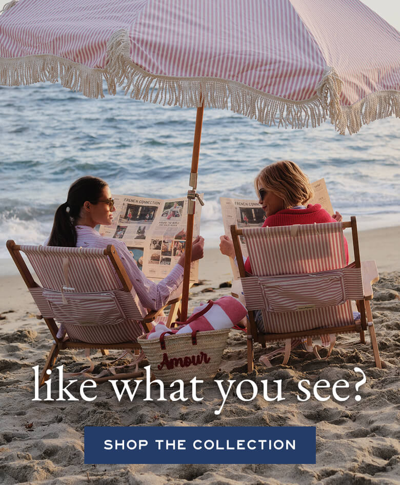 Two women sitting under a striped beach umbrella on the sand with text overlay.