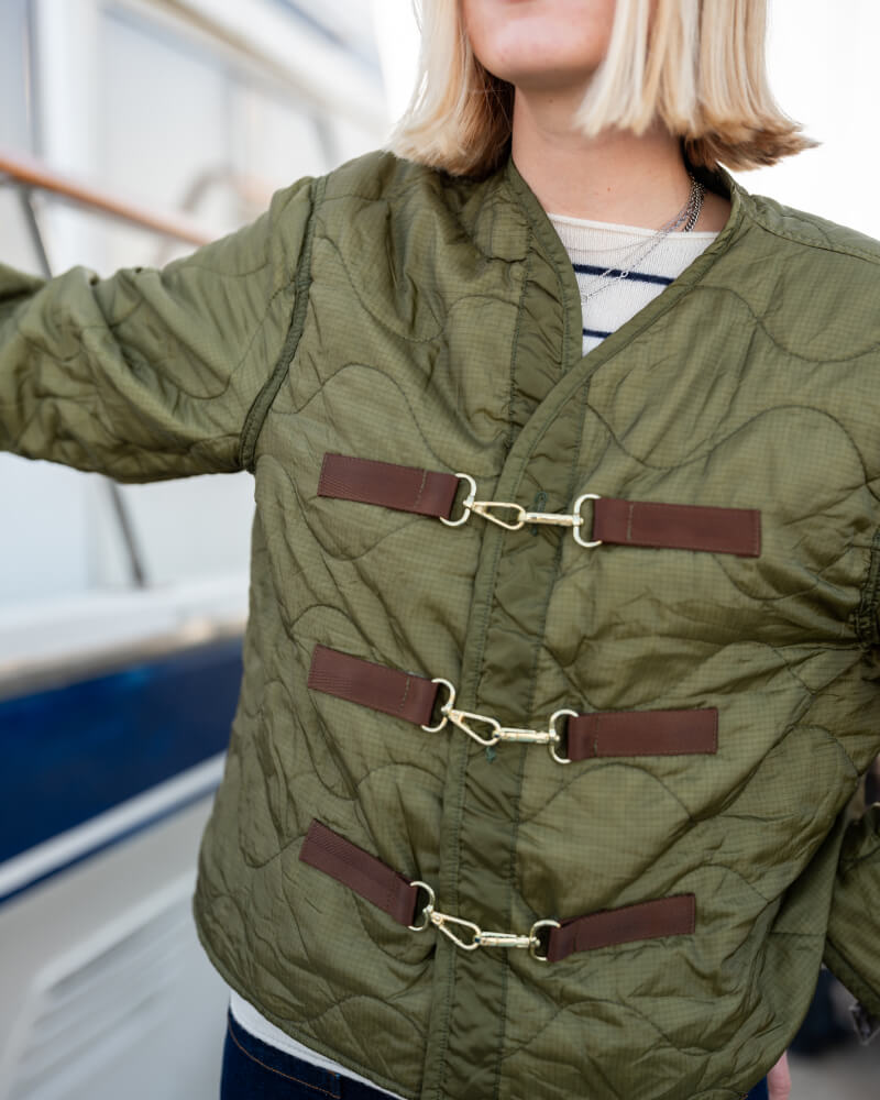 Person wearing a green quilted jacket with brown leather straps in an outdoor setting