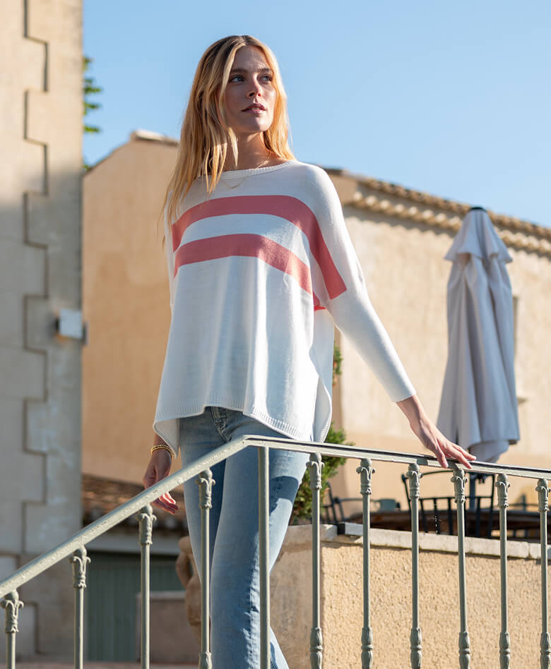 Image of a woman wearing a white sweater with peach stripes.