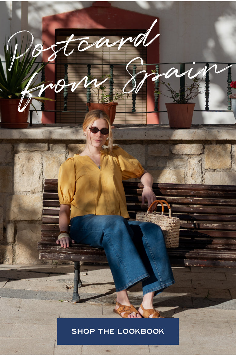 A promotional banner for MERSEA featuring a woman in a mustard yellow shirt and denim pants sitting on a wooden bench against a stone wall. Text: 'Postcard from Spain'