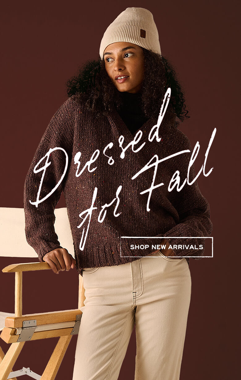 A woman wearing a textured brown sweater and a tan knit beanie, leaning against a chair. Text: 'Dressed for Fall' and 'SHOP NEW ARRIVALS'.