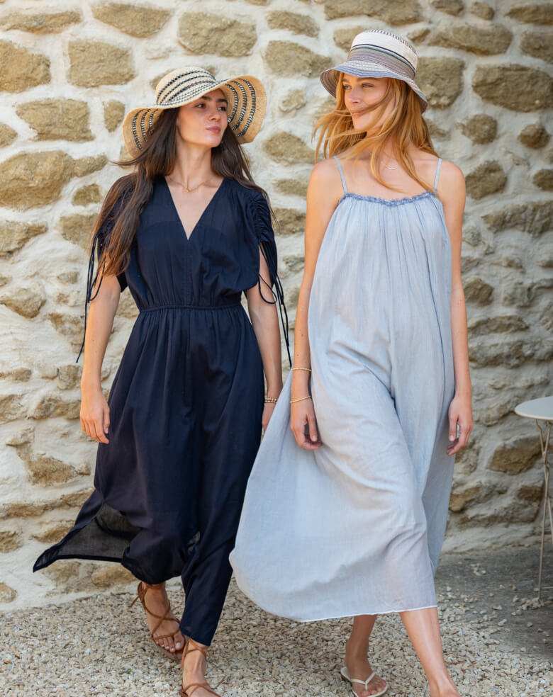 Two women in summer dresses standing against a stone wall.