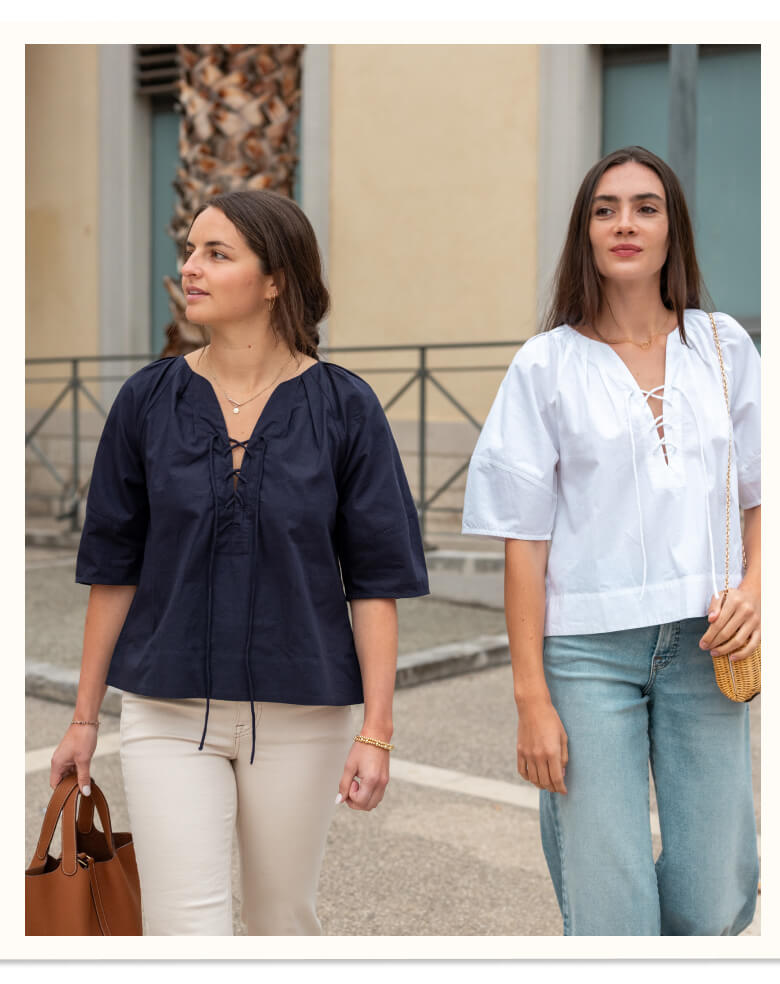 Two women standing outdoors, one in a navy blue top and beige pants, the other in a white top and light blue jeans.