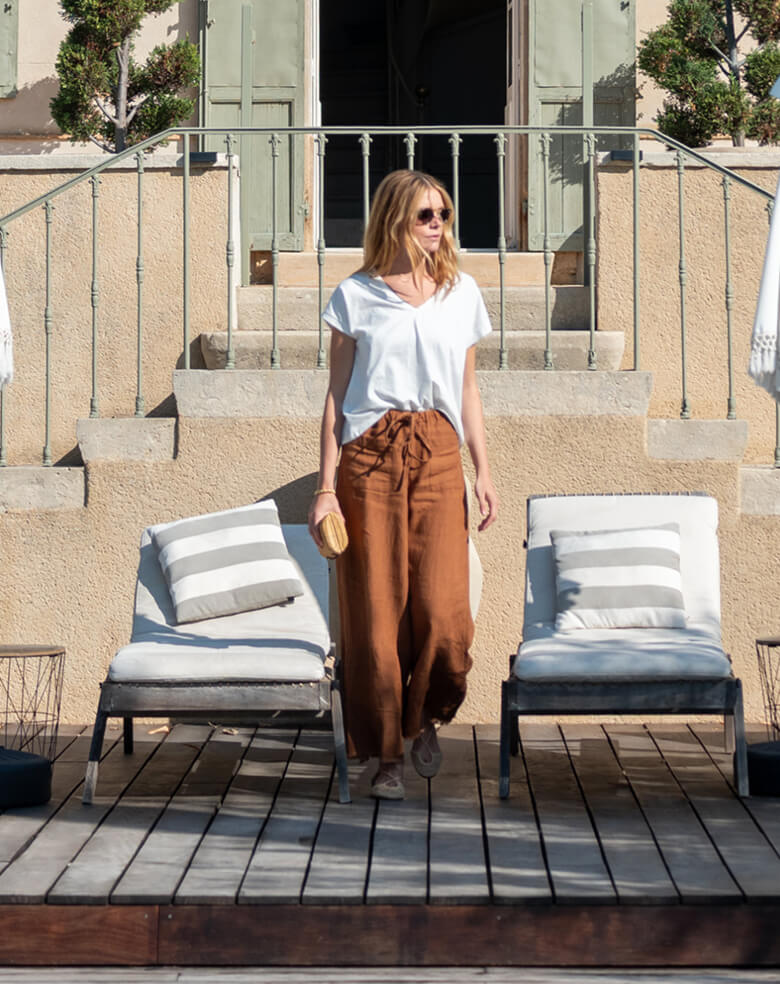 Woman standing on a rooftop deck with lounge chairs and cushions.