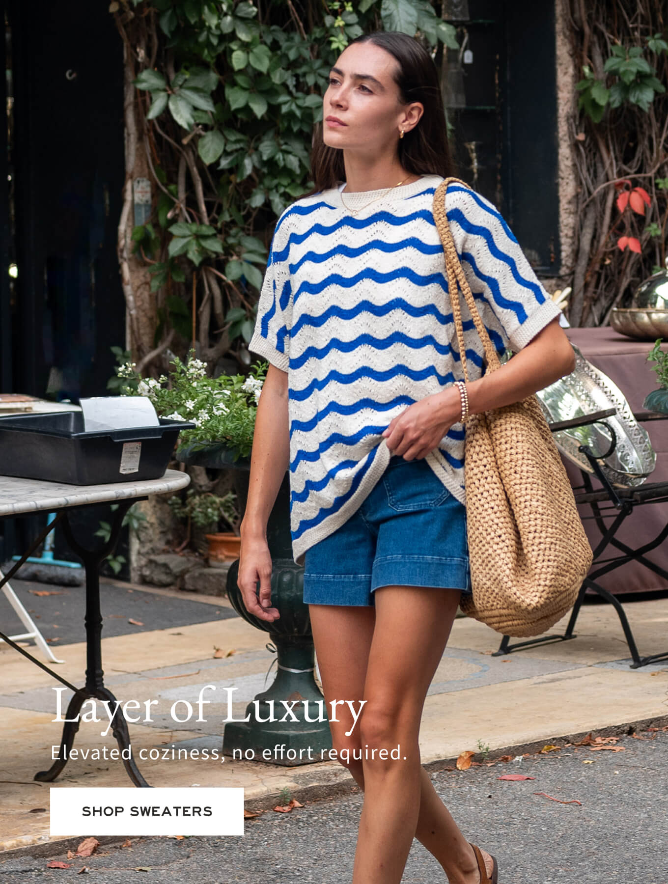 Woman wearing a blue and white striped sweater with denim shorts, walking outdoors.