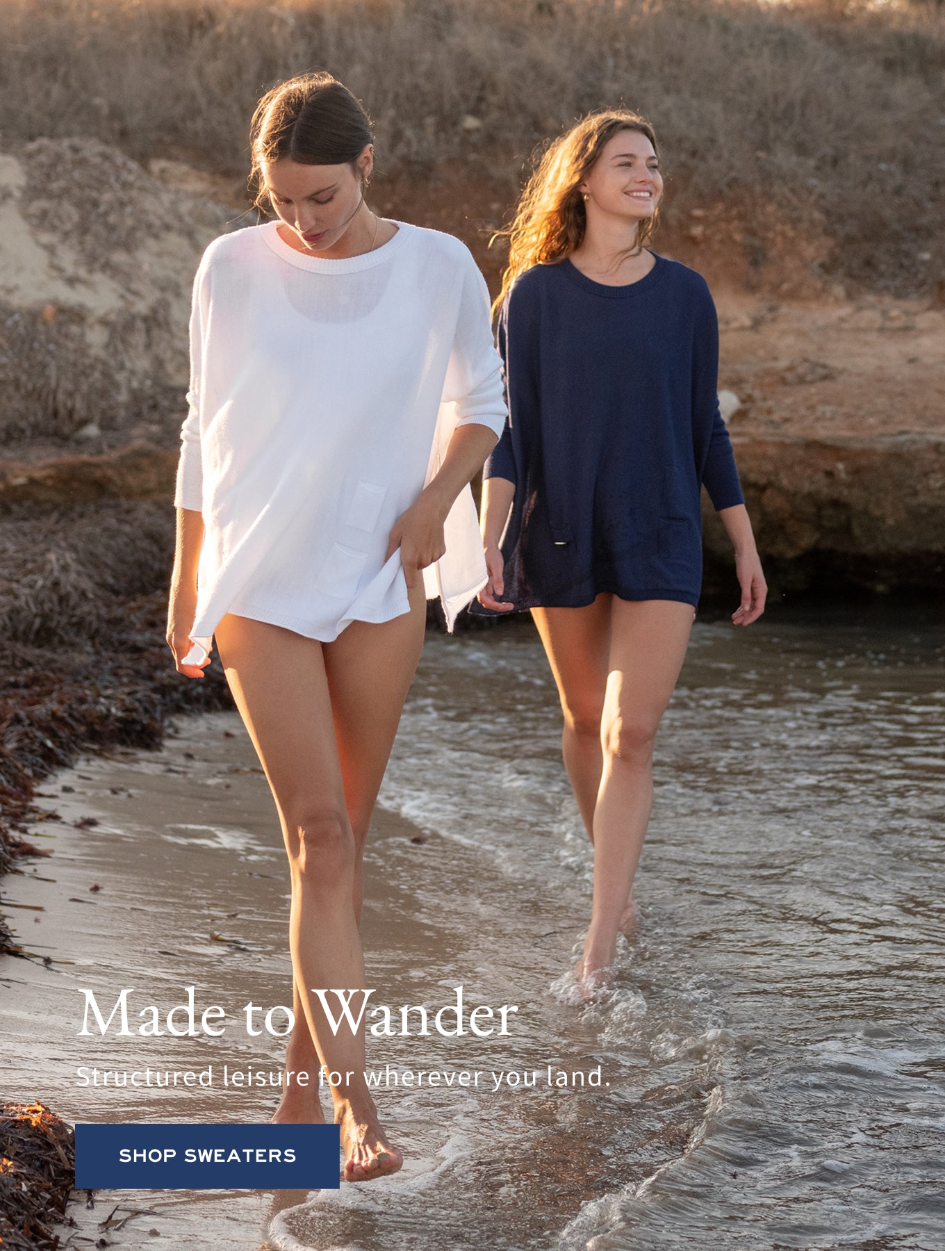 White and navy blue knit sweaters worn by two models walking on a beach. Text: Made to Wander Structured leisure for wherever your land. SHOP SWEATERS