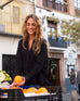 woman wearing black mersea modern oxford tee button down picking up oranges at outdoor market