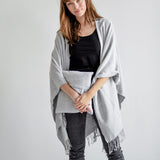 Woman wearing a gray poncho over a black top and jeans on a white background