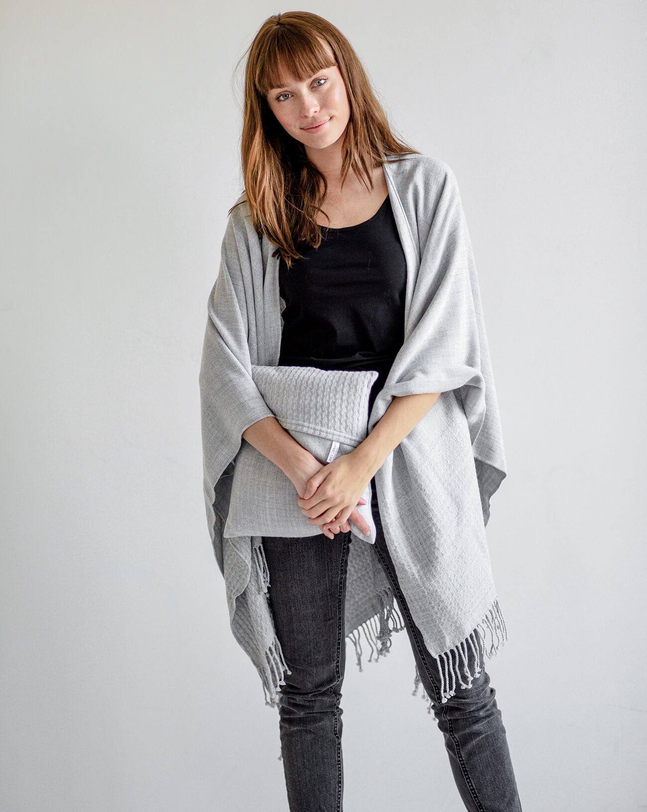 Woman wearing a gray poncho over a black top and jeans on a white background