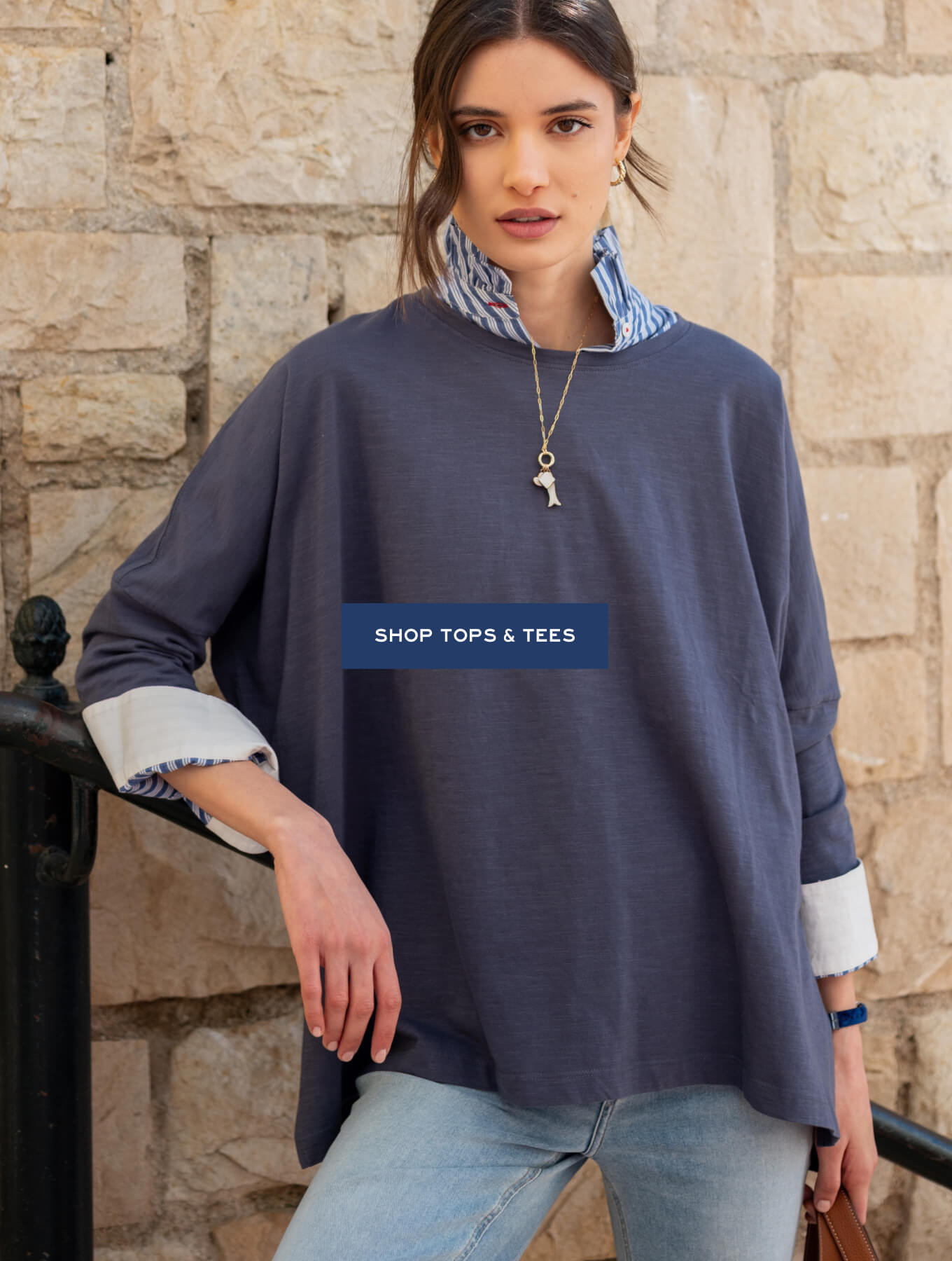 Navy blue oversized knit top with striped fabric underlay and wide cuffs. Text: SHOP TOPS & TEES
