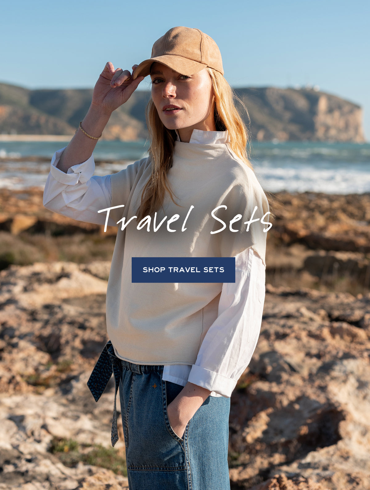 Travel Sets promotional banner featuring a woman in a cream knit top and baseball cap on a rocky beach. Text: 'Travel Sets SHOP TRAVEL SETS'