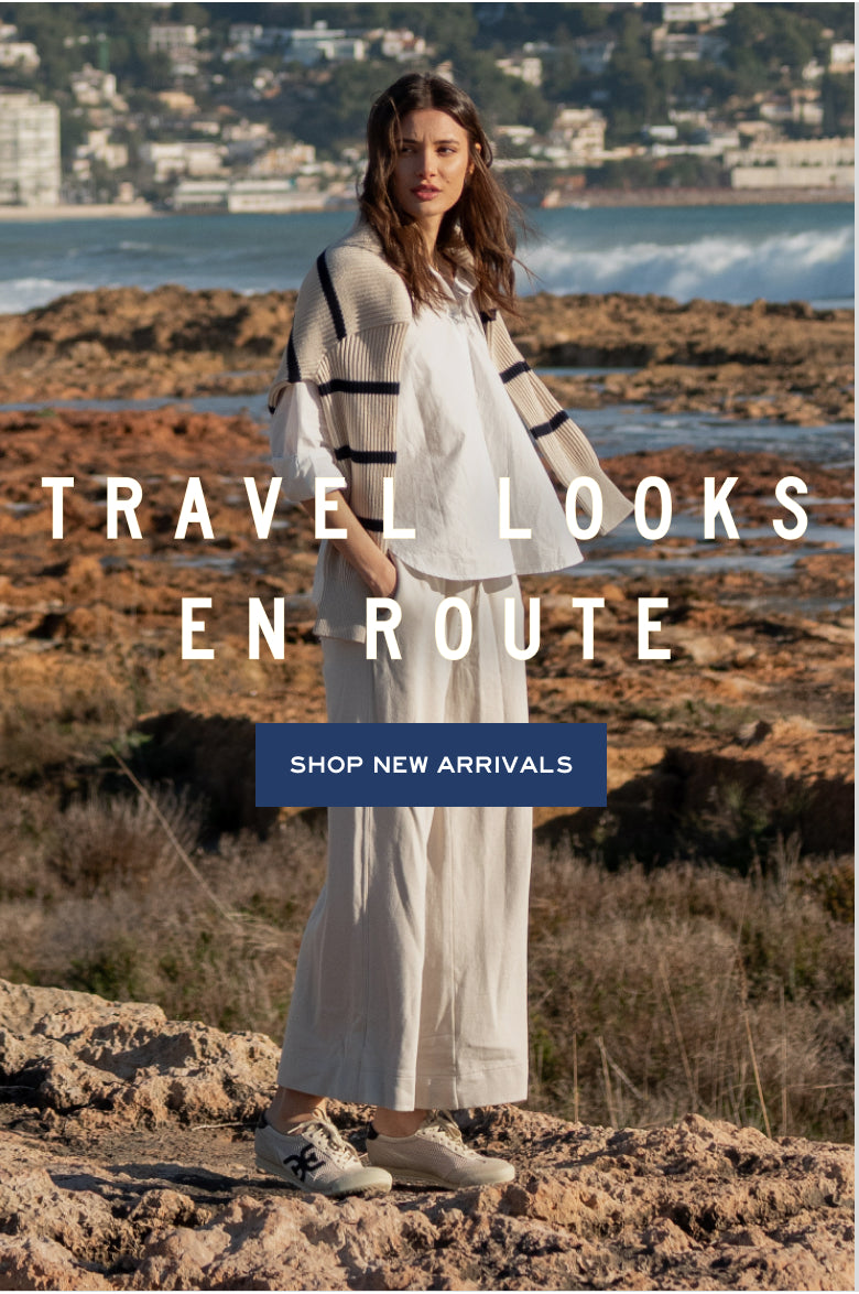 Cream knit ensemble with striped wrap and wide-leg pants. Text: TRAVEL LOOKS EN ROUTE SHOP NEW ARRIVALS
