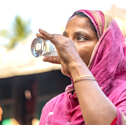 Woman in a pink headscarf drinking water from a clear bottle outdoors.