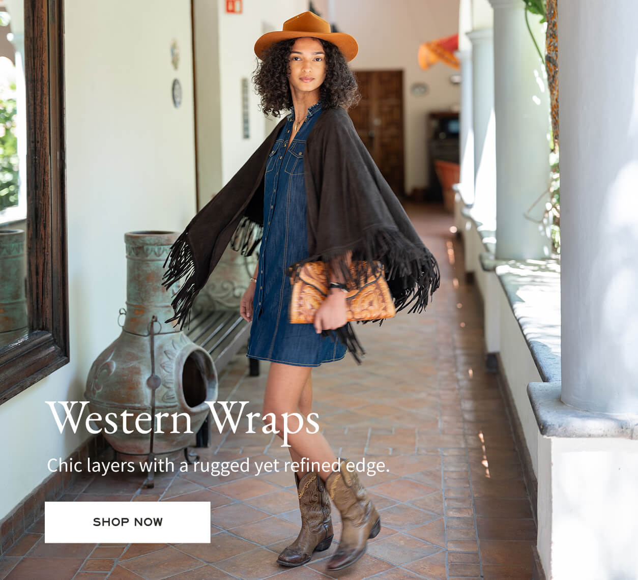 Woman wearing a black fringed wrap, denim dress, and brown boots in an outdoor setting.