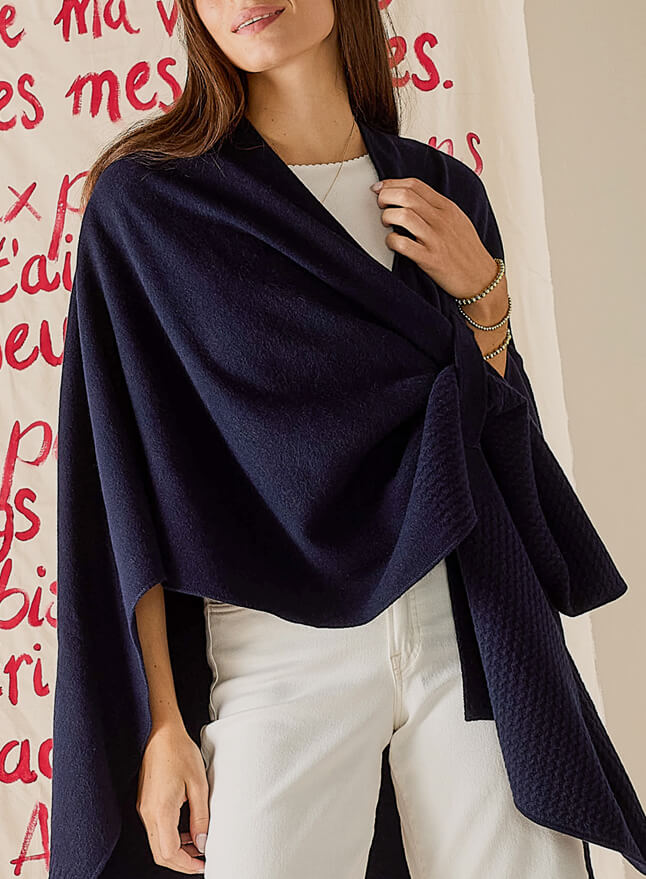 Woman wearing a navy blue shawl over a white outfit against a red text background