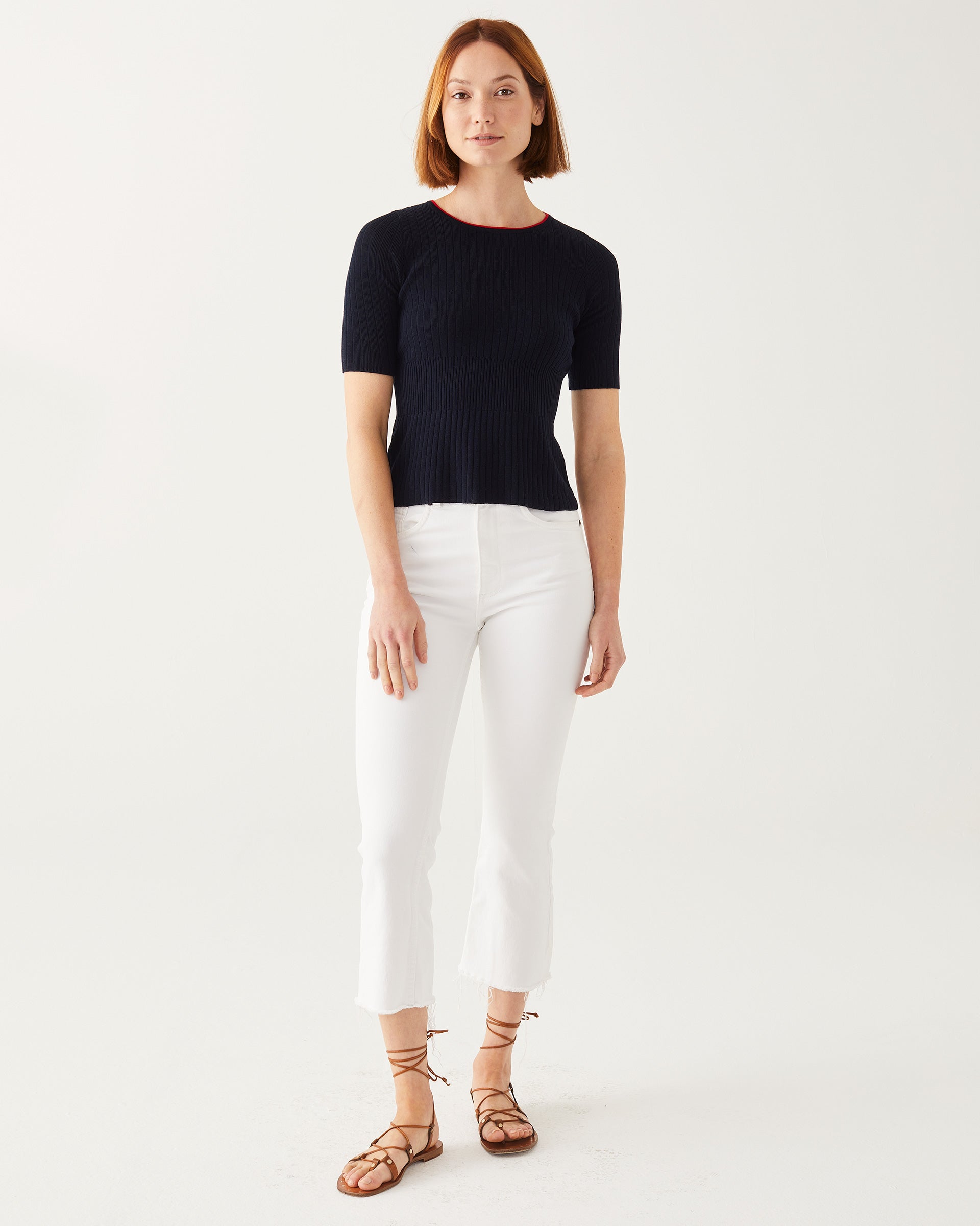 Female wearing white jeans and dark navy top in front of white wall