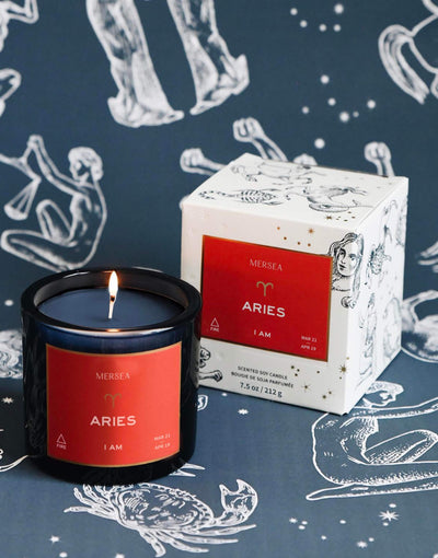 Mersea Aries scented candle displayed beside its accompanying box, set against an astrology sign-themed backdrop