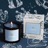 Mersea Cancer scented candle displayed beside its accompanying box, set against an astrology sign-themed backdrop